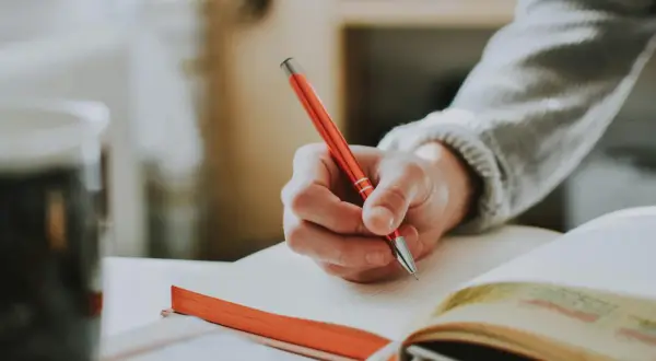 Mano escribiendo en un cuaderno con ejercicios de tiempos verbales en español.