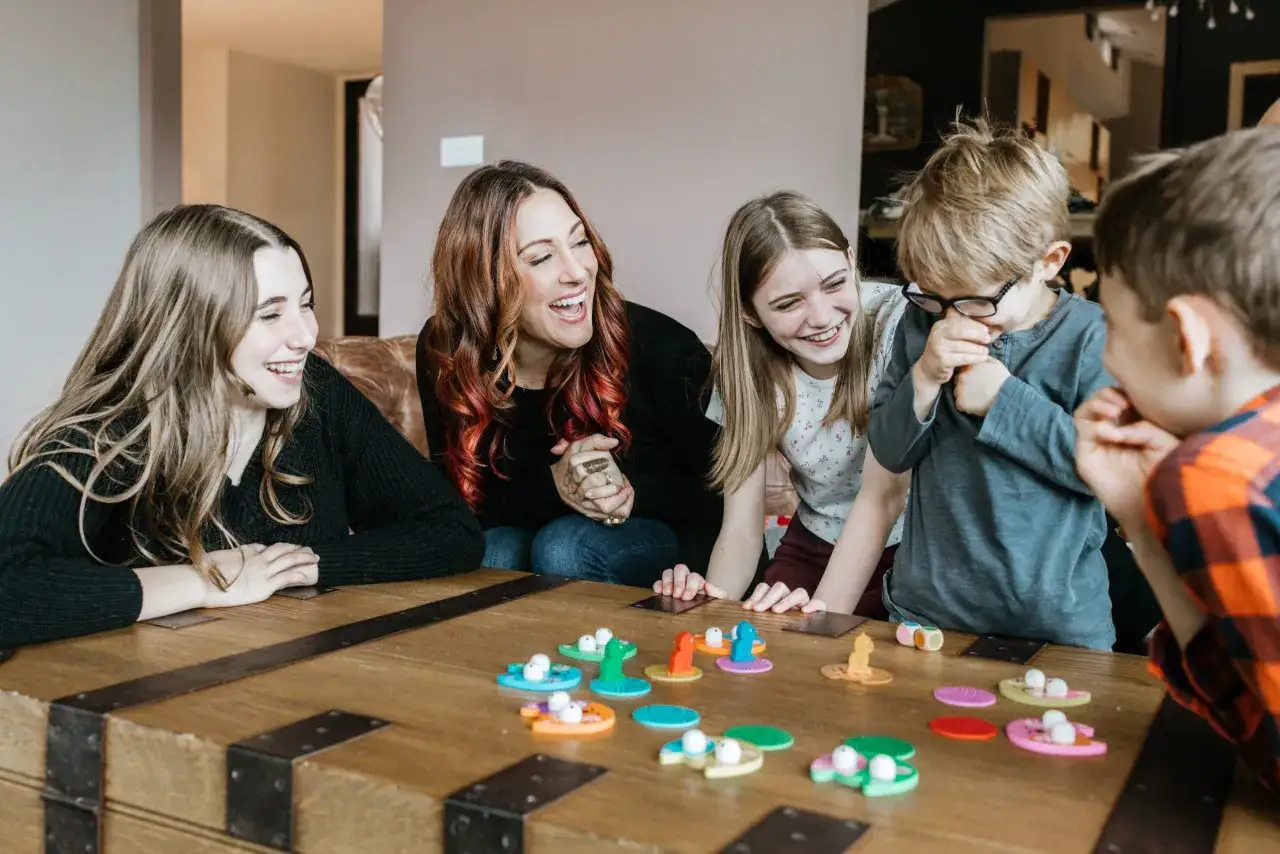 Familia riendo mientras juega un juego de mesa con coloridas piezas. Las preguntas para ni&ntilde;os parecen ser el tema.
