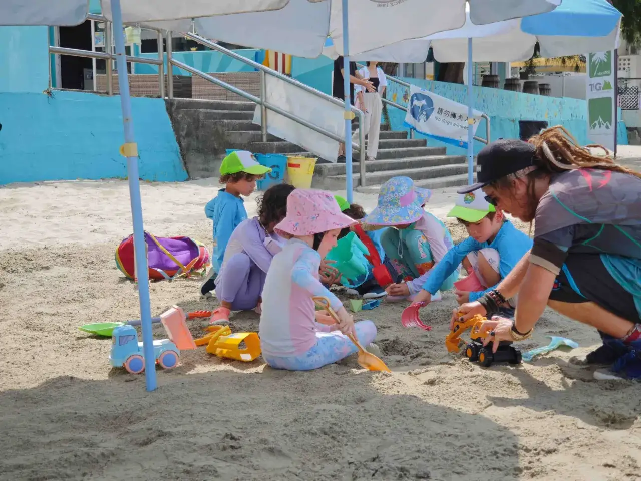 Niños disfrutan de juegos en la playa sin material, construyendo con arena y juguetes.