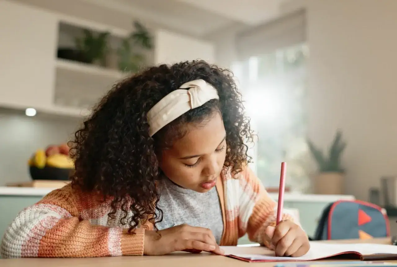 Ni&ntilde;a concentrada en su dictado de 2 primaria, escribiendo con un l&aacute;piz rosa.