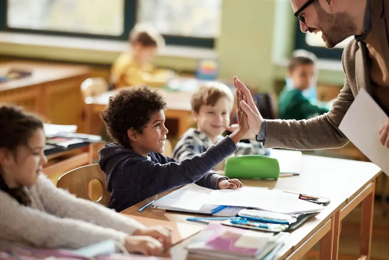 Maestro da un cinco a un niño en clase. Un ejemplo de crianza en positivo, fomentando la confianza y el éxito en el aprendizaje.
