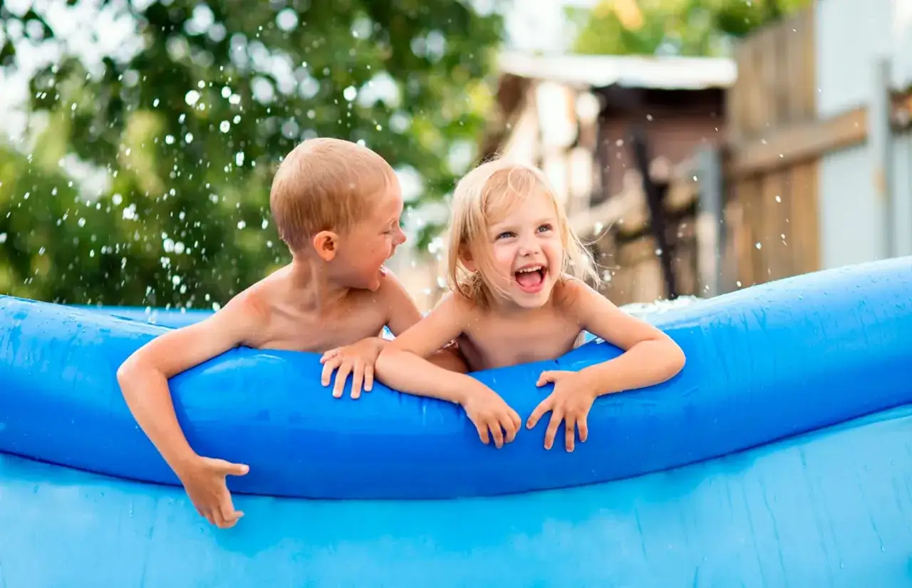 Ni&ntilde;os riendo y chapoteando en una piscina inflable azul, disfrutando de juegos refrescantes.