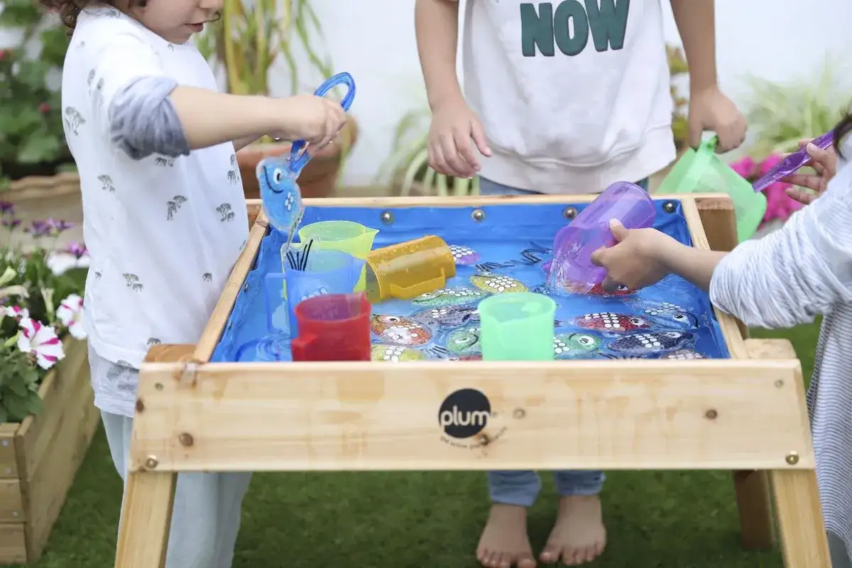 Ni&ntilde;os jugando con peces de juguete en una mesa de agua, como si estuvieran en la playa.