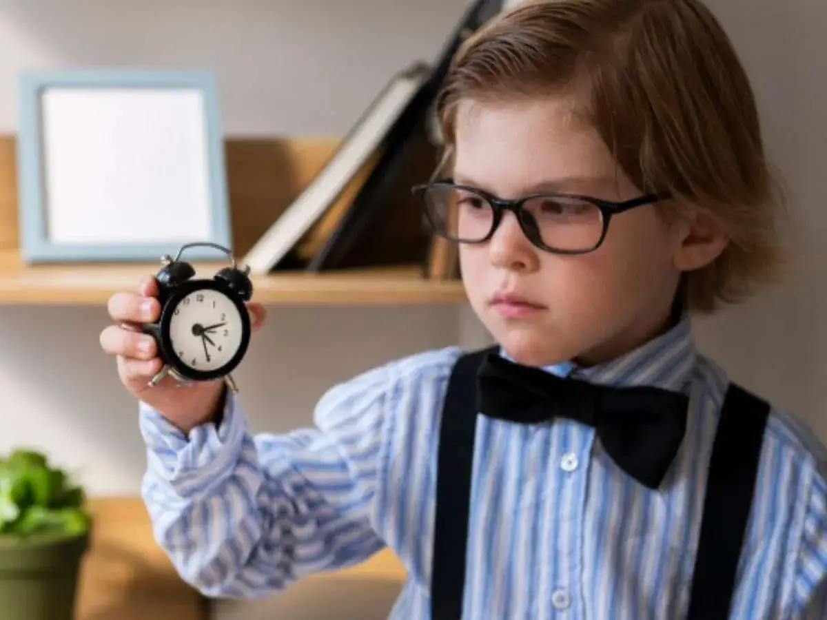 Ni&ntilde;o con gafas y pajarita sostiene un despertador. Son las horas en punto y media, &iexcl;hora de aprender!