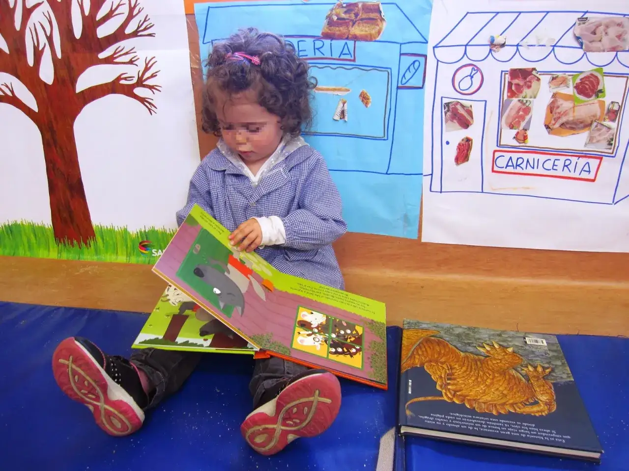 Niña con rizos lee un cuento sobre un lobo y conejos. Detrás, un dibujo de una carnicería.