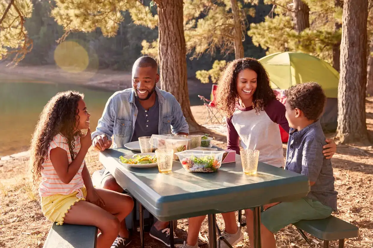 Familia disfrutando de un picnic al aire libre, con comida y risas. Un d&iacute;a perfecto para actividades dia de la familia junto al lago.