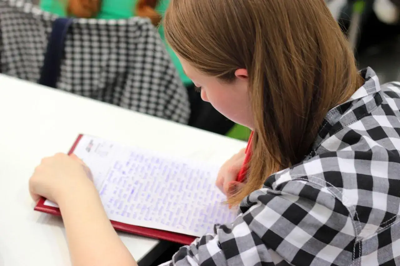 Chica concentrada en su dictado 1 eso, escribiendo en un cuaderno con bolígrafo rojo.